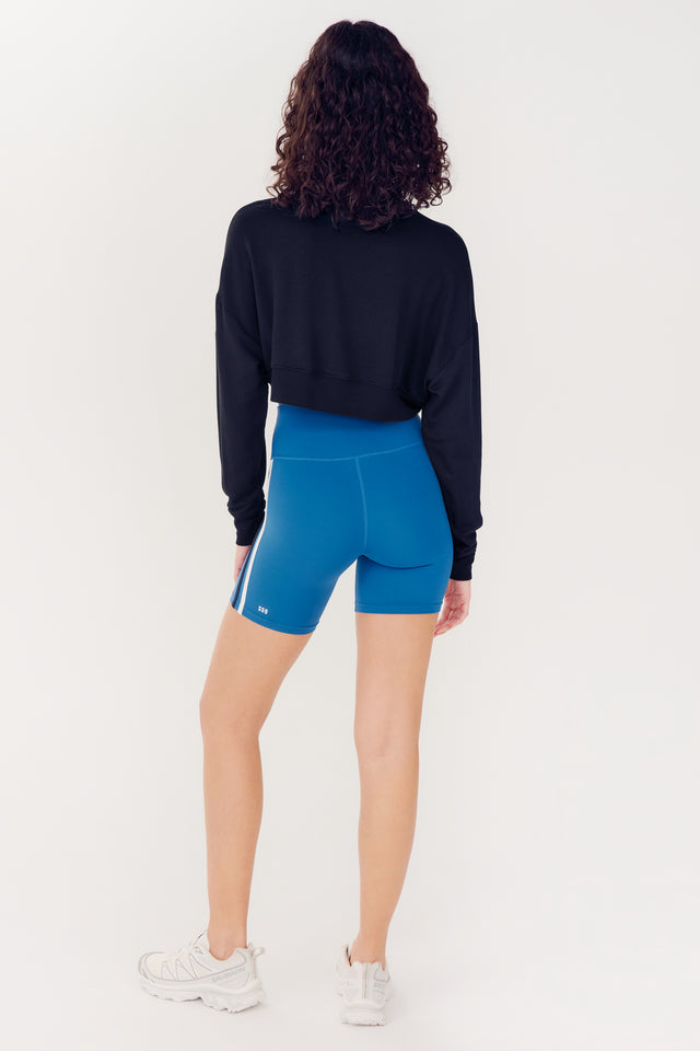 Woman in blue shorts and SPLITS59 Noah Fleece Crop Sweatshirt - Black viewed from behind against a white background.