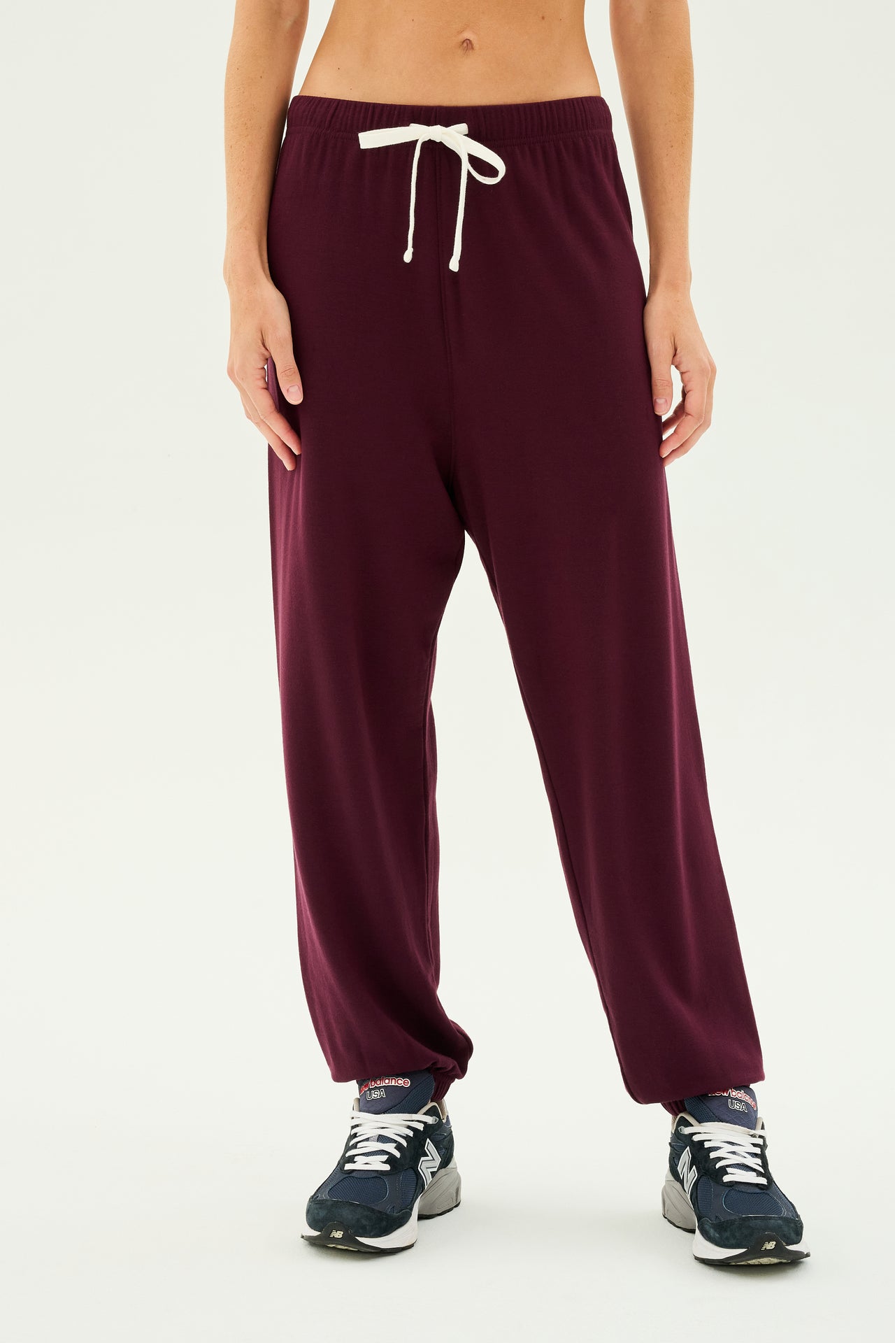 Person wearing SPLITS59 Andie Oversized Fleece Sweatpant in Dark Cherry with a white drawstring, standing in blue sneakers against a plain white background. Perfect for cool weather workouts.