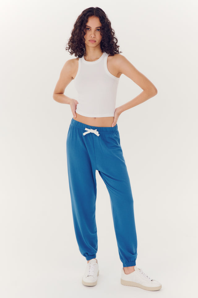 Woman posing in a white tank top made of spandex and Andie Oversized Fleece Sweatpant - Stone Blue by SPLITS59 against a white background.