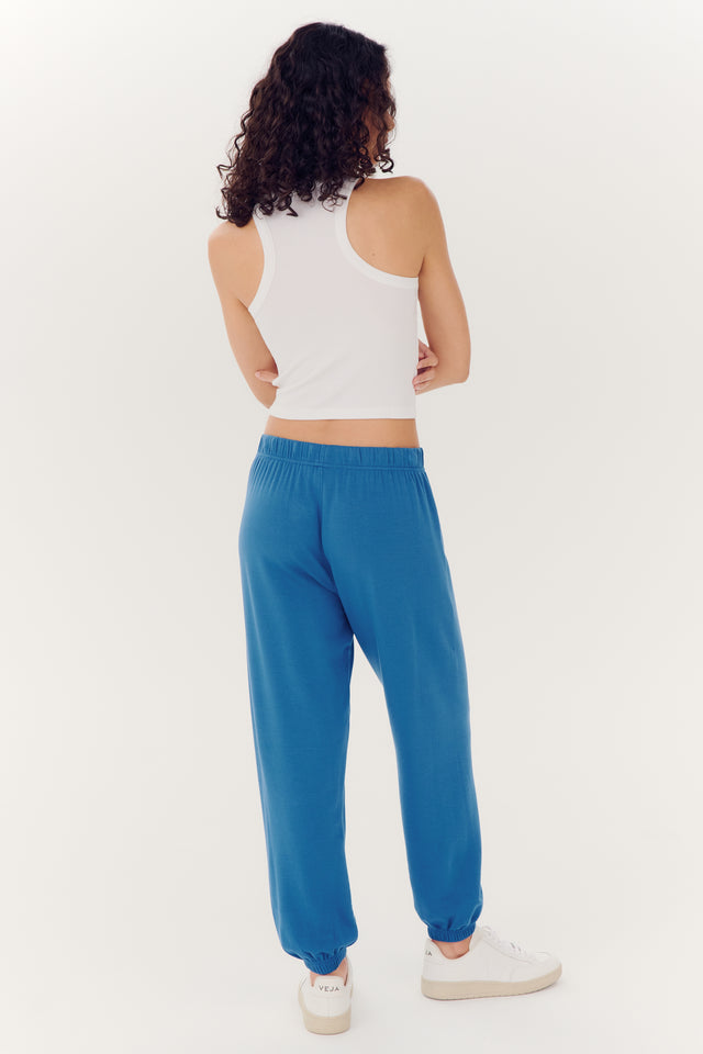 Woman standing with her back to the camera wearing SPLITS59 Andie Oversized Fleece Sweatpant - Stone Blue and a white tank top made of Spandex fabric.