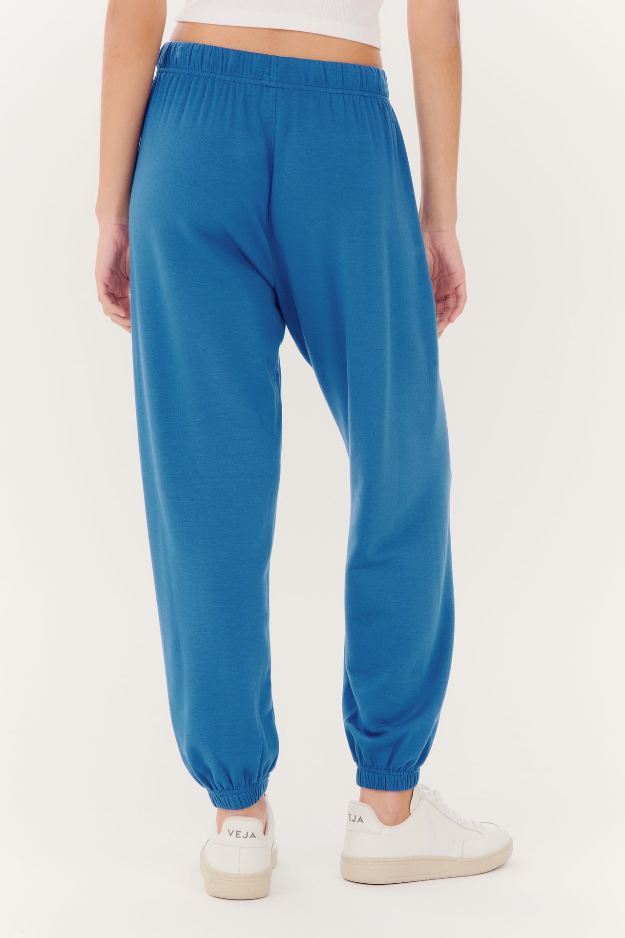 A person standing, showcasing SPLITS59 Andie Oversized Fleece Sweatpant - Stone Blue made of modal fabric and white sneakers.