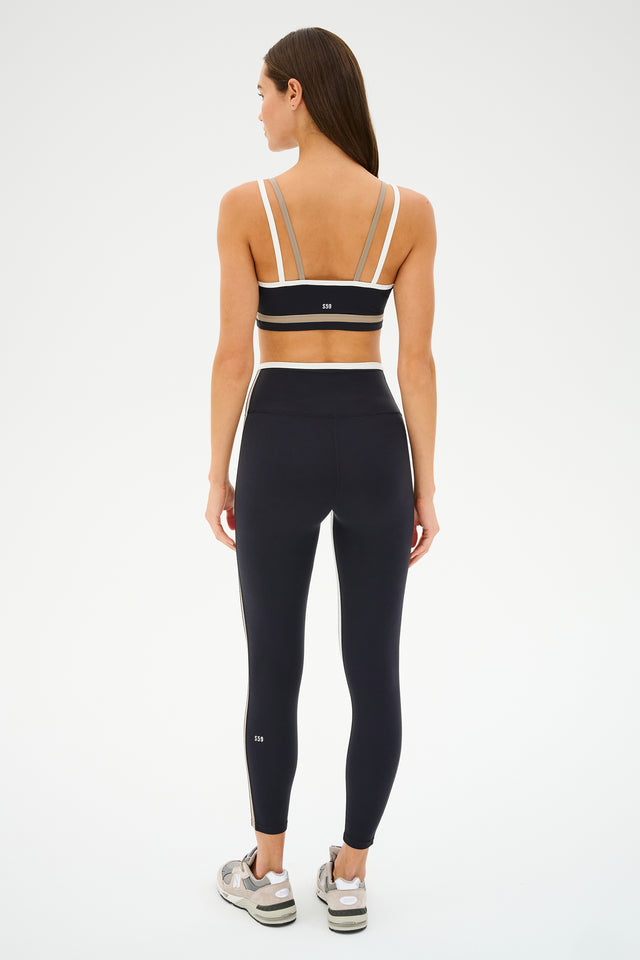 Someone is seen from the back in a black SPLITS59 Eva Rigor Double Strap Bra - Black/Latte and leggings, with subtle contrast color details, against a plain white background.