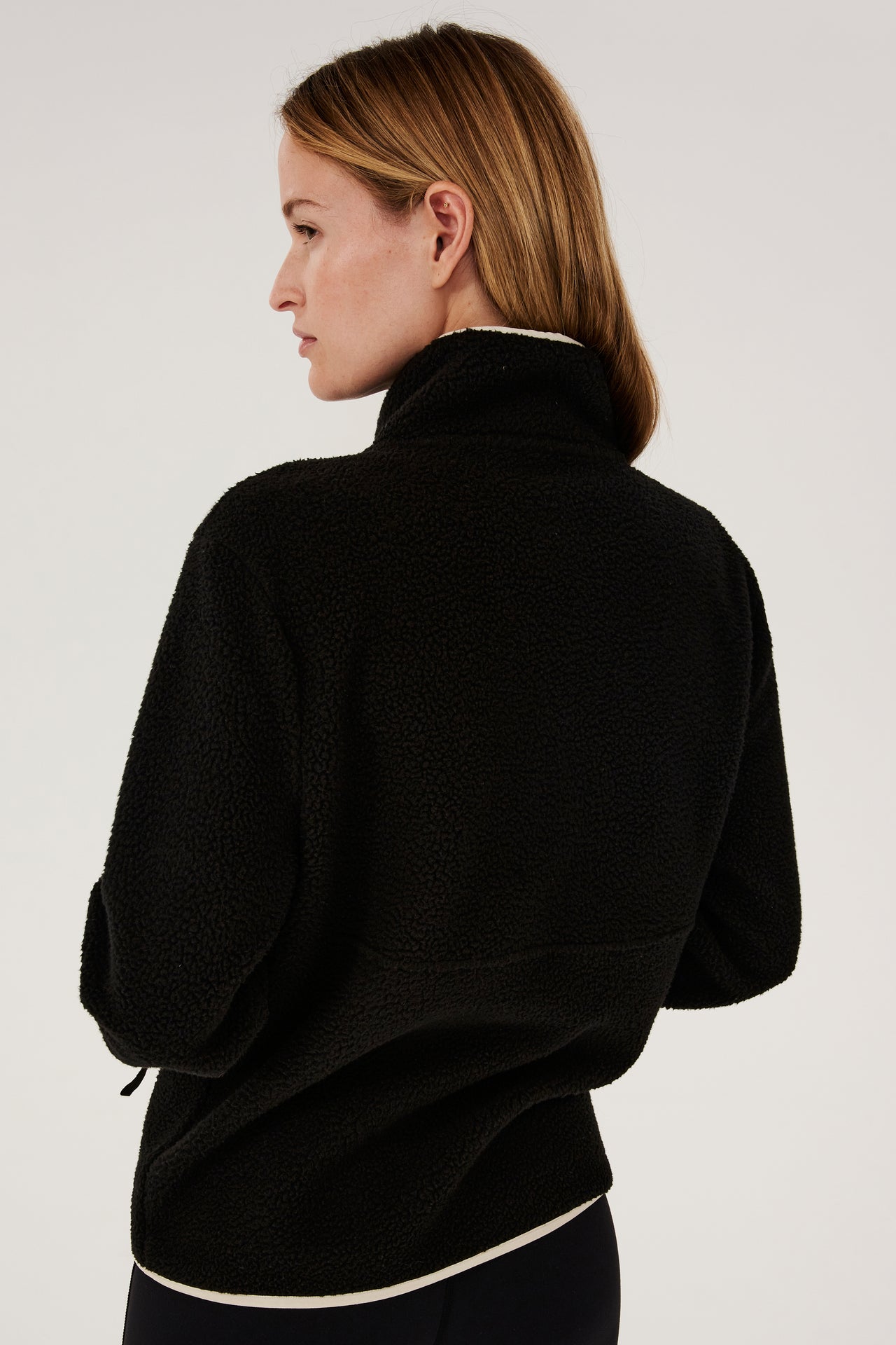The back view of a woman wearing a SPLITS59 Libby Sherpa Half Zip in Black/Creme.