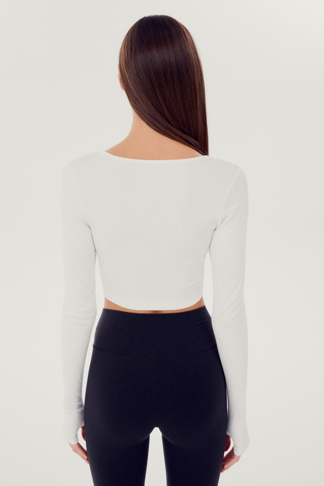 The back view of a woman wearing black leggings and a SPLITS59 Rene Rib Crop Cardigan in white, ready for her gym workouts.