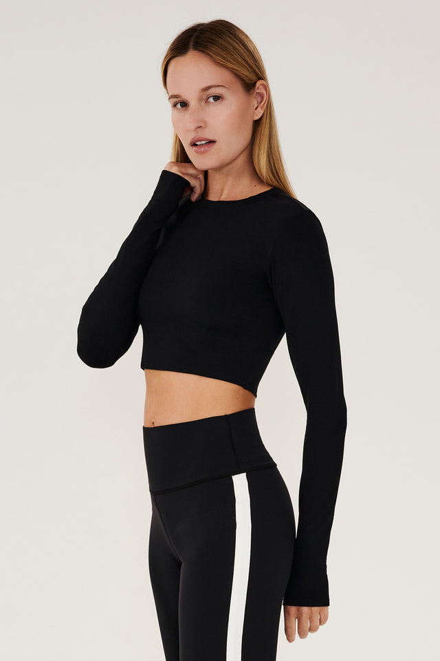 Side view of girl wearing black long sleeve crop top and black leggings with white stripe