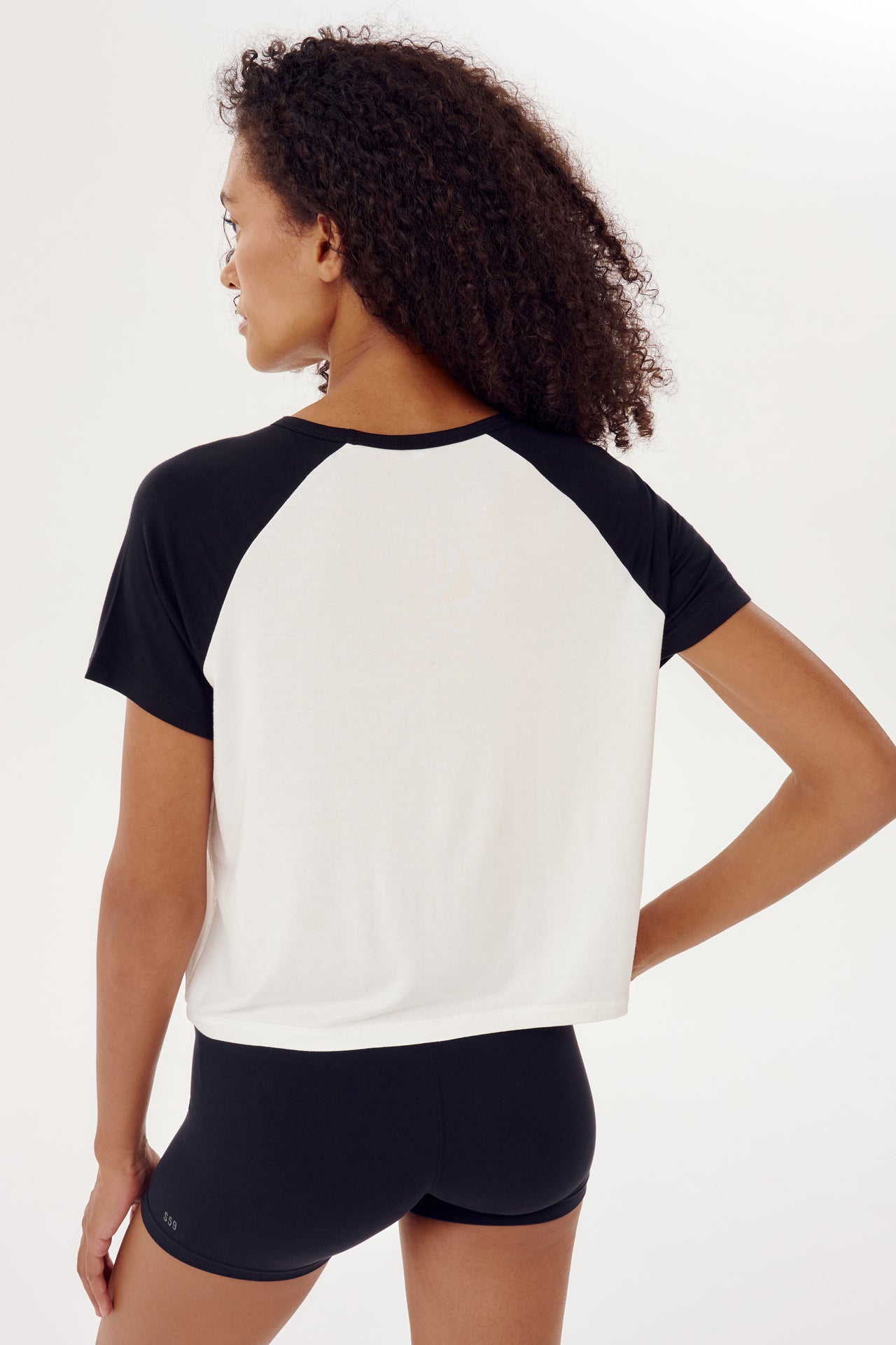 The back view of a woman wearing a SPLITS59 Baseball Jersey Tee in White/Black, perfect for relaxed fit gym workouts.