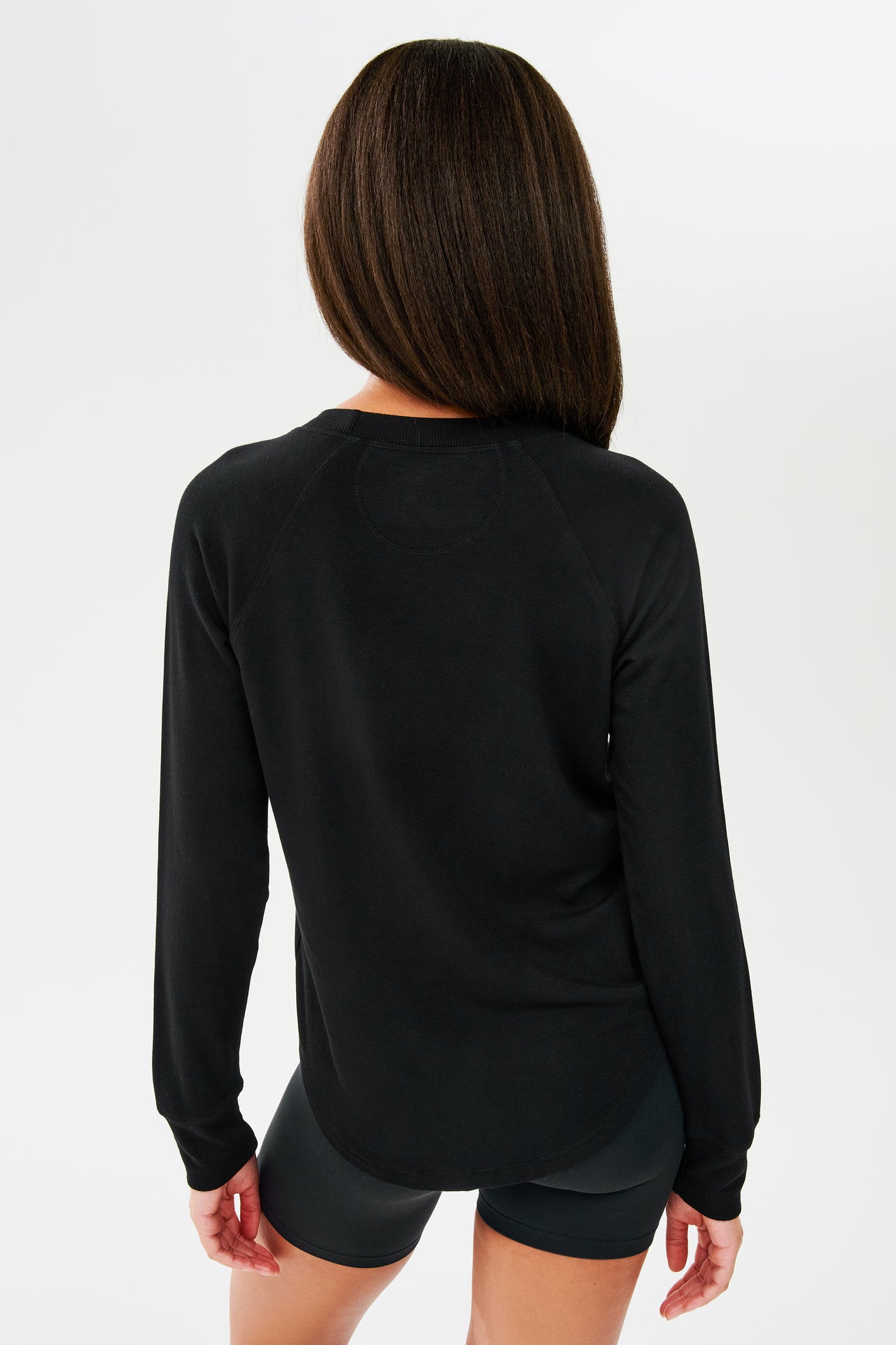 Back side shot of woman with dark straight hair, wearing black sweatshirt with black shorts