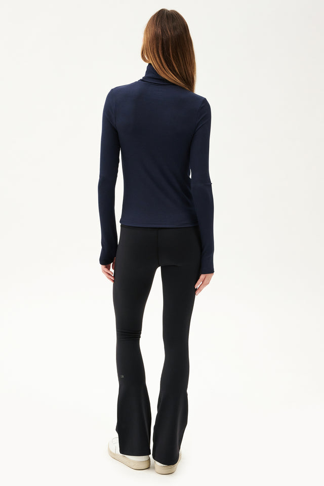The back view of a woman wearing black leggings and a Jackson Rib Full Length Turtleneck in Indigo by SPLITS59, perfect for yoga.