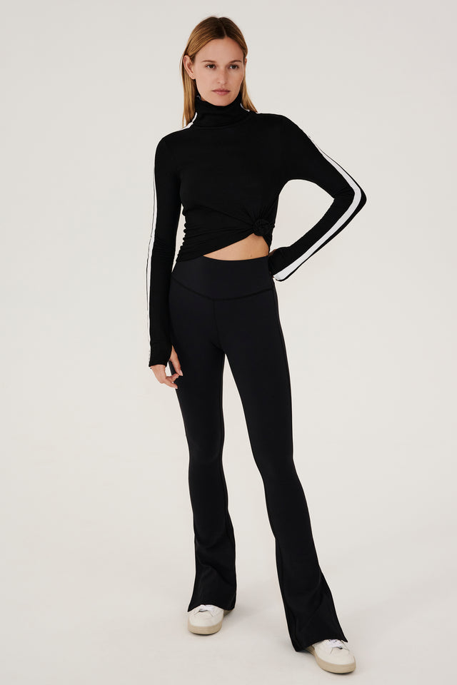 The model is wearing a black SPLITS59 Jackson Rib Full Length Turtleneck top and flared leggings, designed for substantial coverage during running.