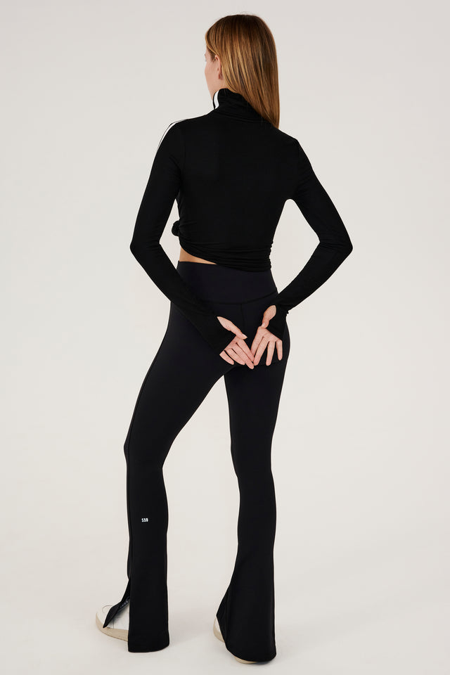 The back view of a woman wearing black flared leggings and a SPLITS59 Jackson Rib Full Length Turtleneck, designed for enhanced coverage while running.