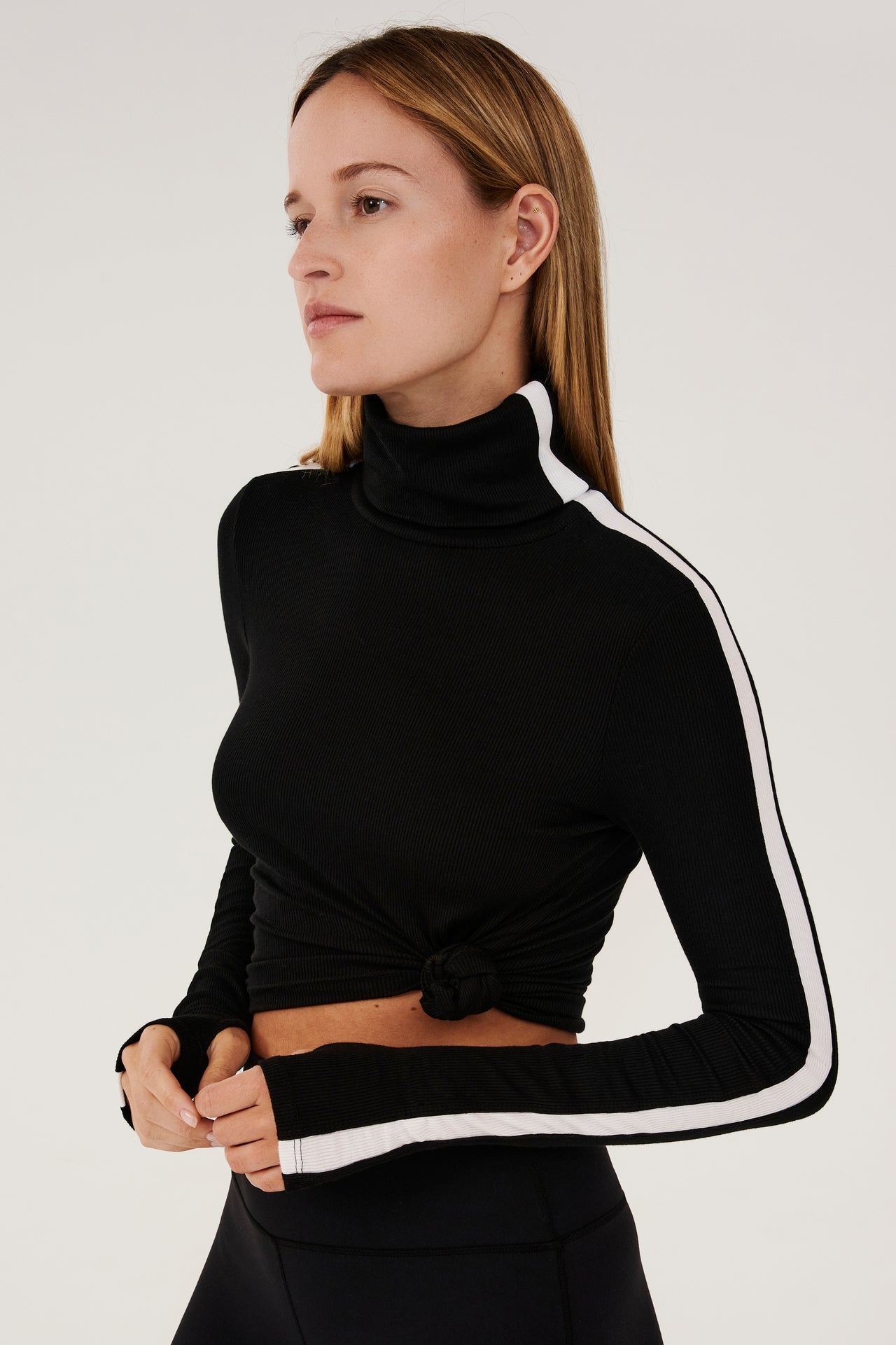 A woman wearing a black SPLITS59 Jackson Rib Full Length Turtleneck top and white leggings designed for running with enhanced coverage.