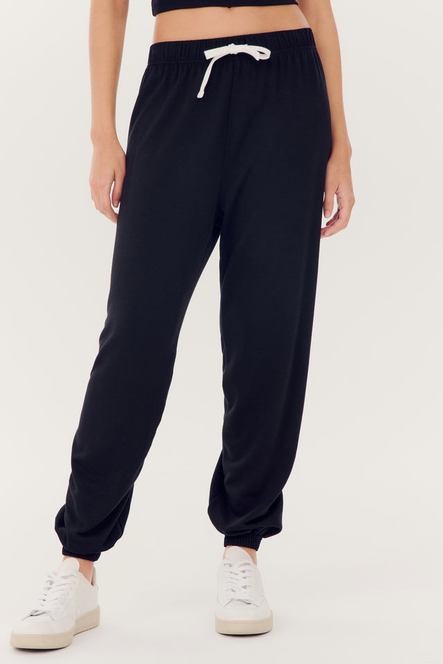 A person wearing SPLITS59 Andie Oversized Fleece Sweatpant in Black and white sneakers.