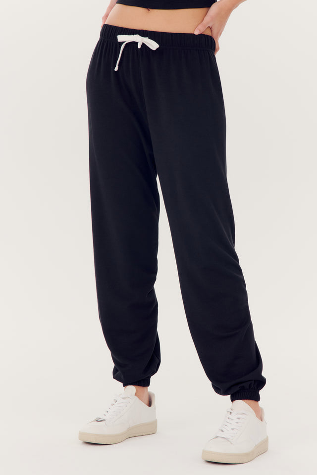 Person wearing Andie Oversized Fleece Sweatpant in black modal spandex blend and white sneakers.