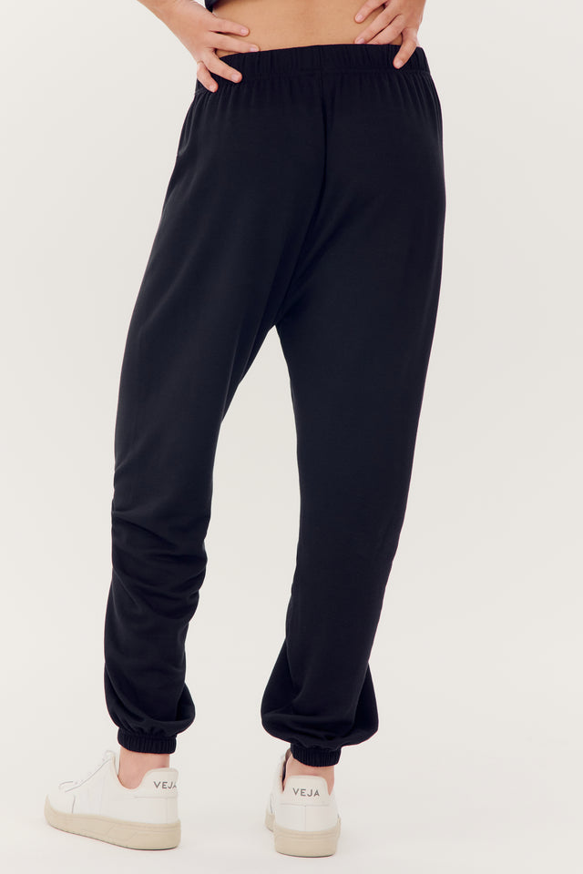 A person standing in SPLITS59 Andie Oversized Fleece Sweatpants in black made of modal fabric and spandex, paired with white sneakers.