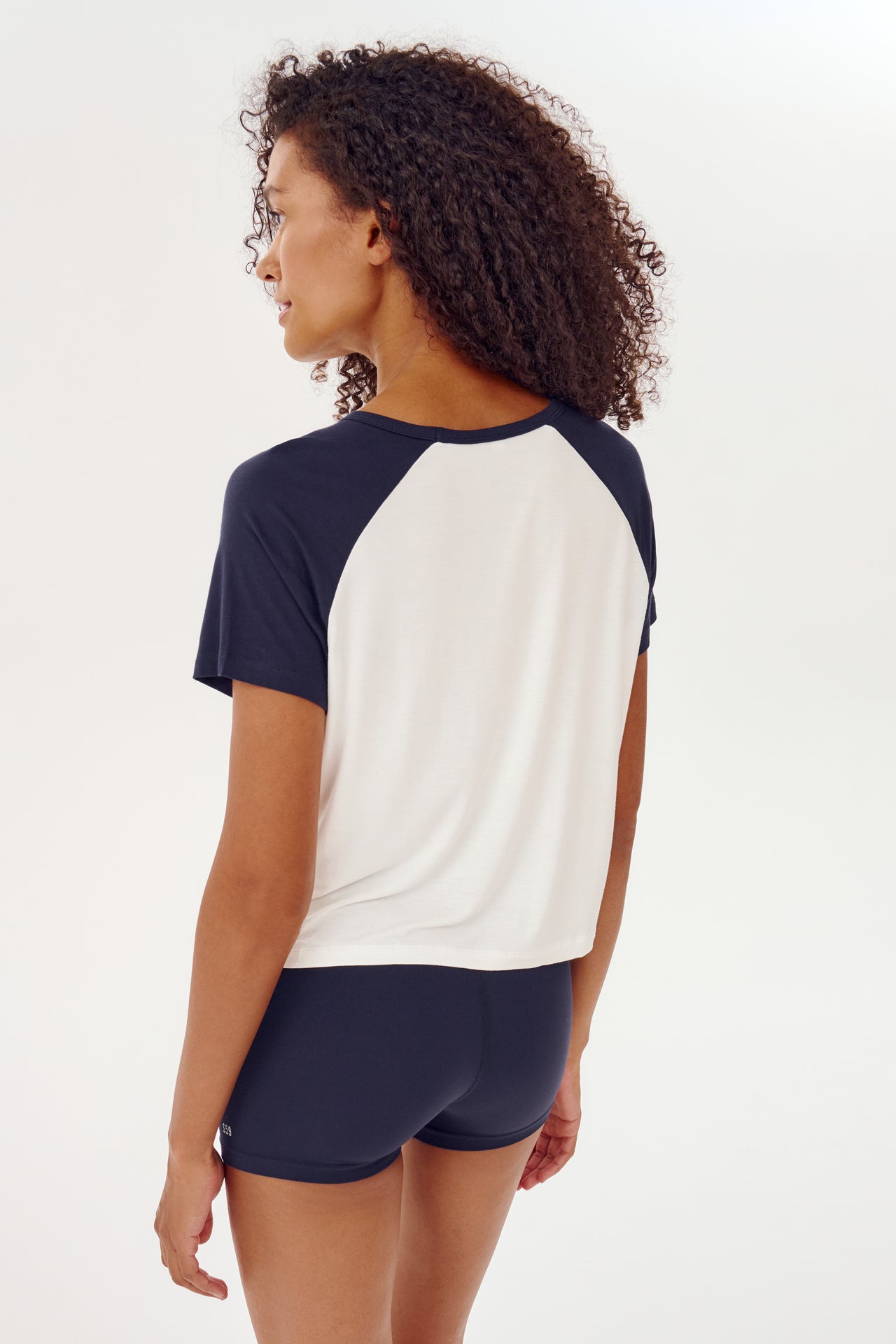 The back view of a woman wearing a SPLITS59 white and indigo baseball jersey tee, ready for her CrossFit gym workouts.