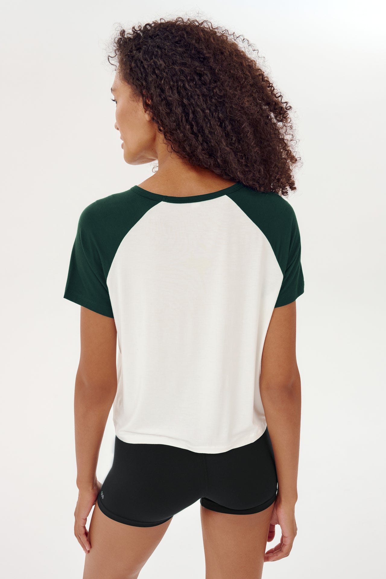 The back view of a woman wearing a SPLITS59 Baseball Jersey Tee in White/Forest with a relaxed fit.