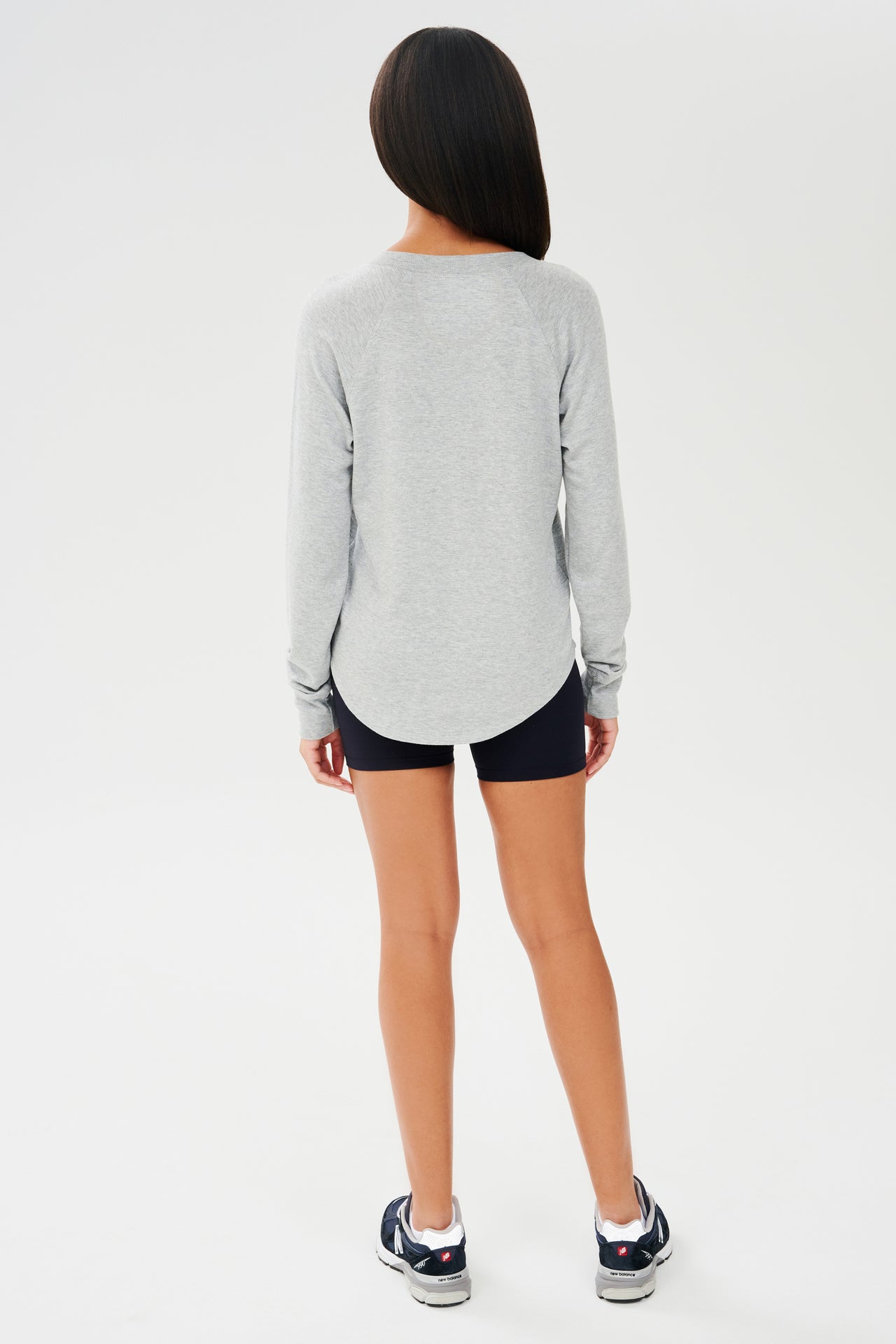 Full back side shot of woman with dark straight hair, wearing grey sweatshirt with black shorts and dark blue shoes