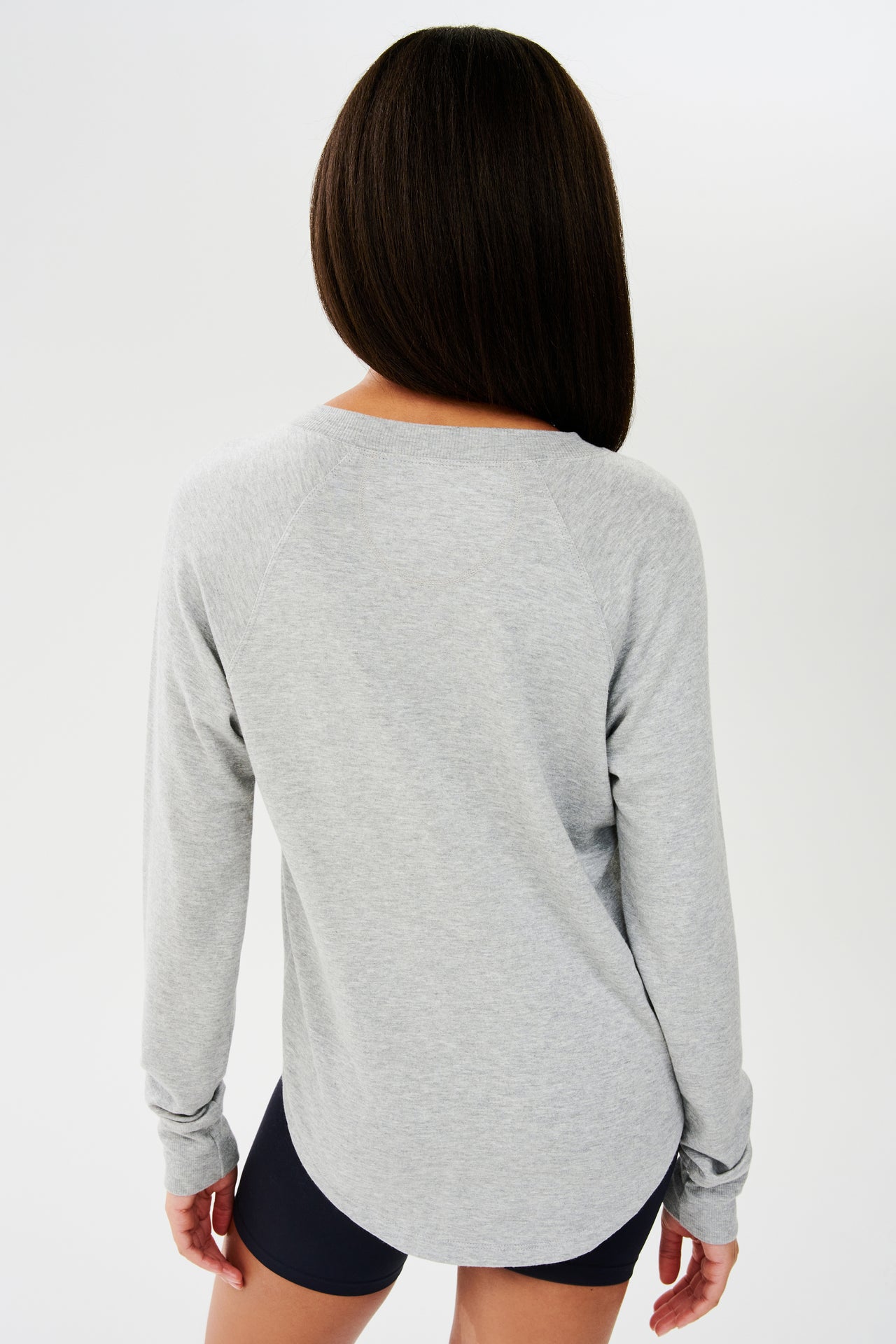 Back side shot of woman with dark straight hair, wearing grey sweatshirt with black shorts