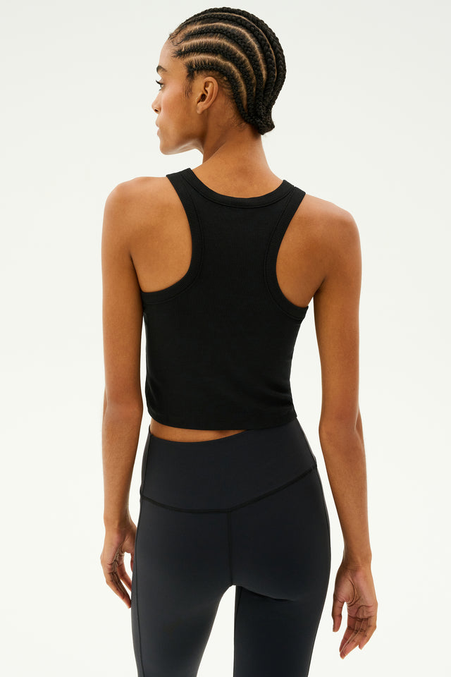 A person wearing a SPLITS59 Kiki Rib Crop Tank in black and leggings made in Los Angeles is viewed from the back against a light background.