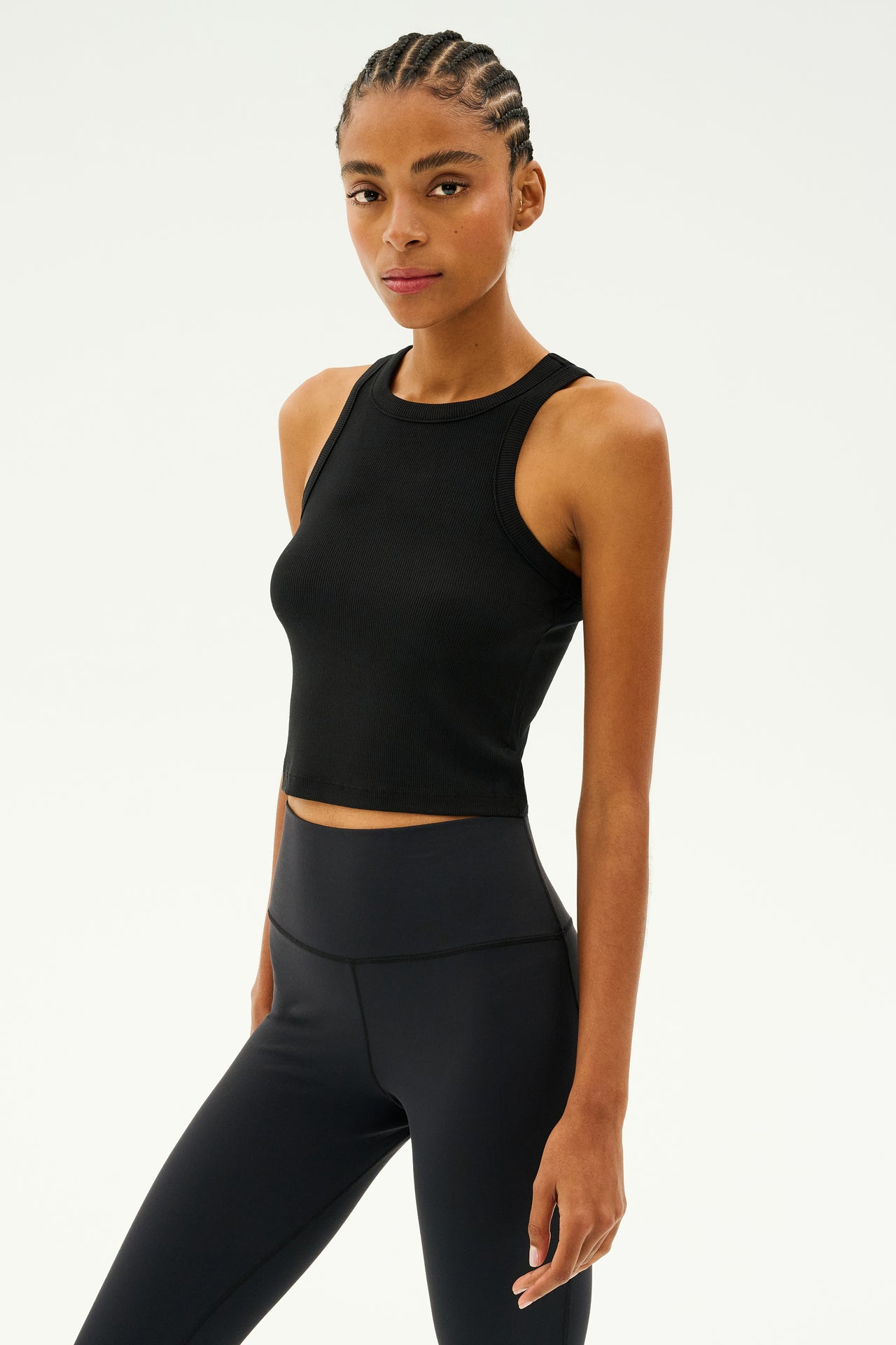 A person with braided hair is styled in the black Kiki Rib Crop Tank by SPLITS59 and leggings, standing against a plain background.