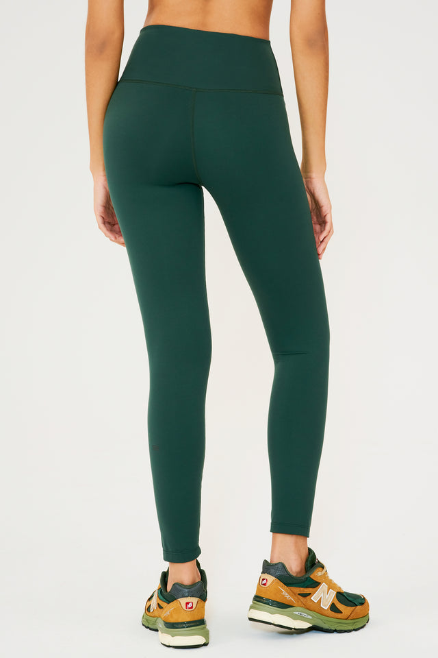 Back view of model wearing dark green high waist  leggings and paired with dark green and orange shoes