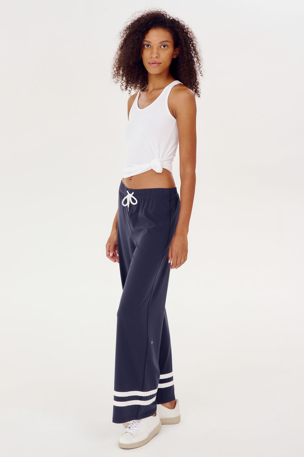 The model is wearing a comfortable white top and SPLITS59 navy Quinn Airweight Wide Leg Pants, ideal for a yoga or workout session.