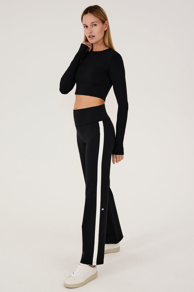 The model is wearing a black crop top and SPLITS59 white Harper Supplex Pant with a side stripe.