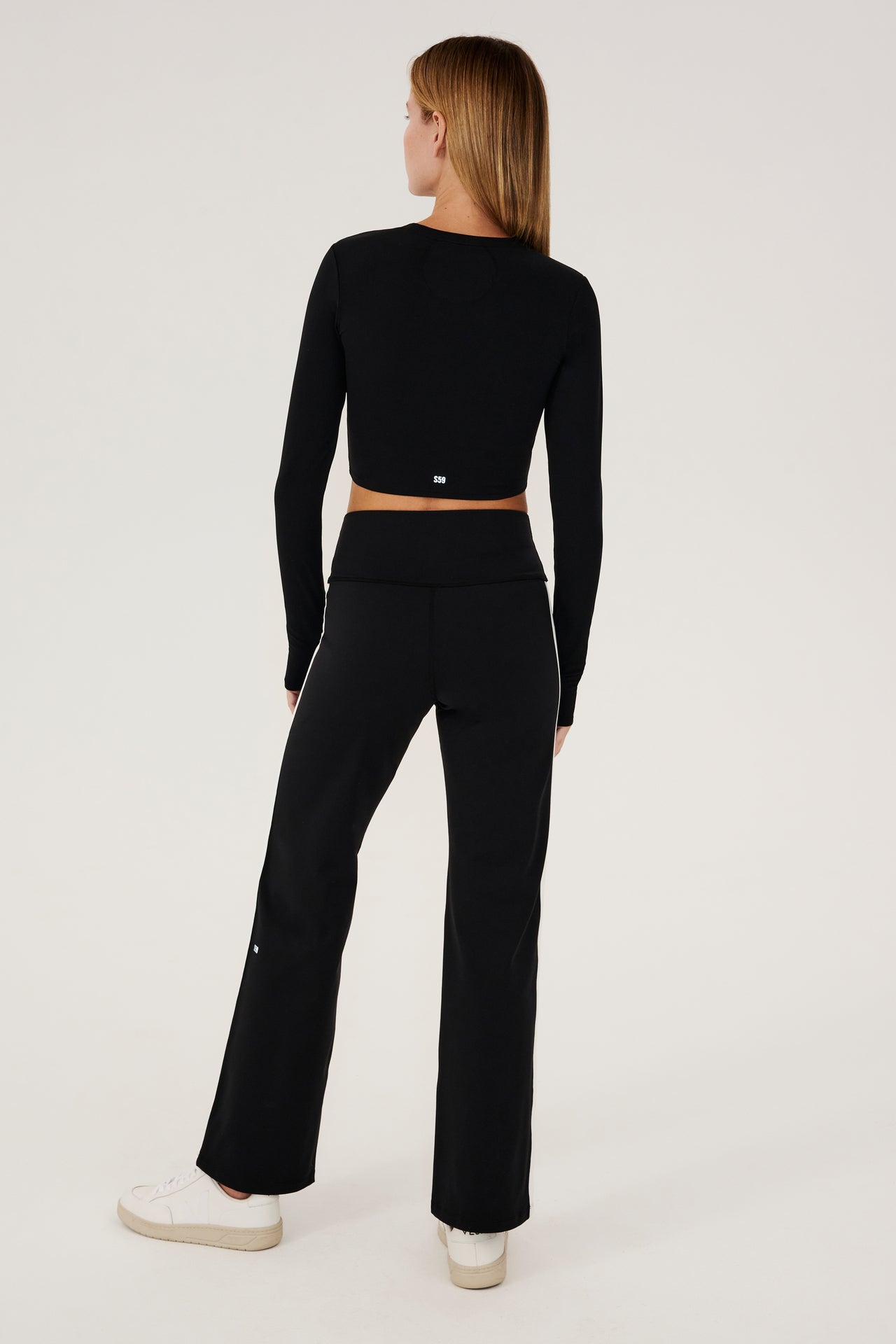 The back view of a woman wearing a SPLITS59 Harper Supplex Pant in Black/White and leggings with a side stripe.