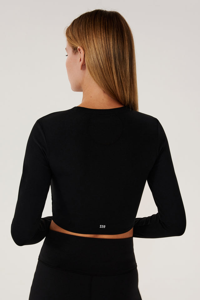 Back view of girl wearing black long sleeve crop top and black leggings 