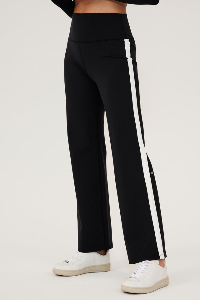 A woman wearing SPLITS59's Harper Supplex Pant in Black/White with a side stripe and white sneakers.