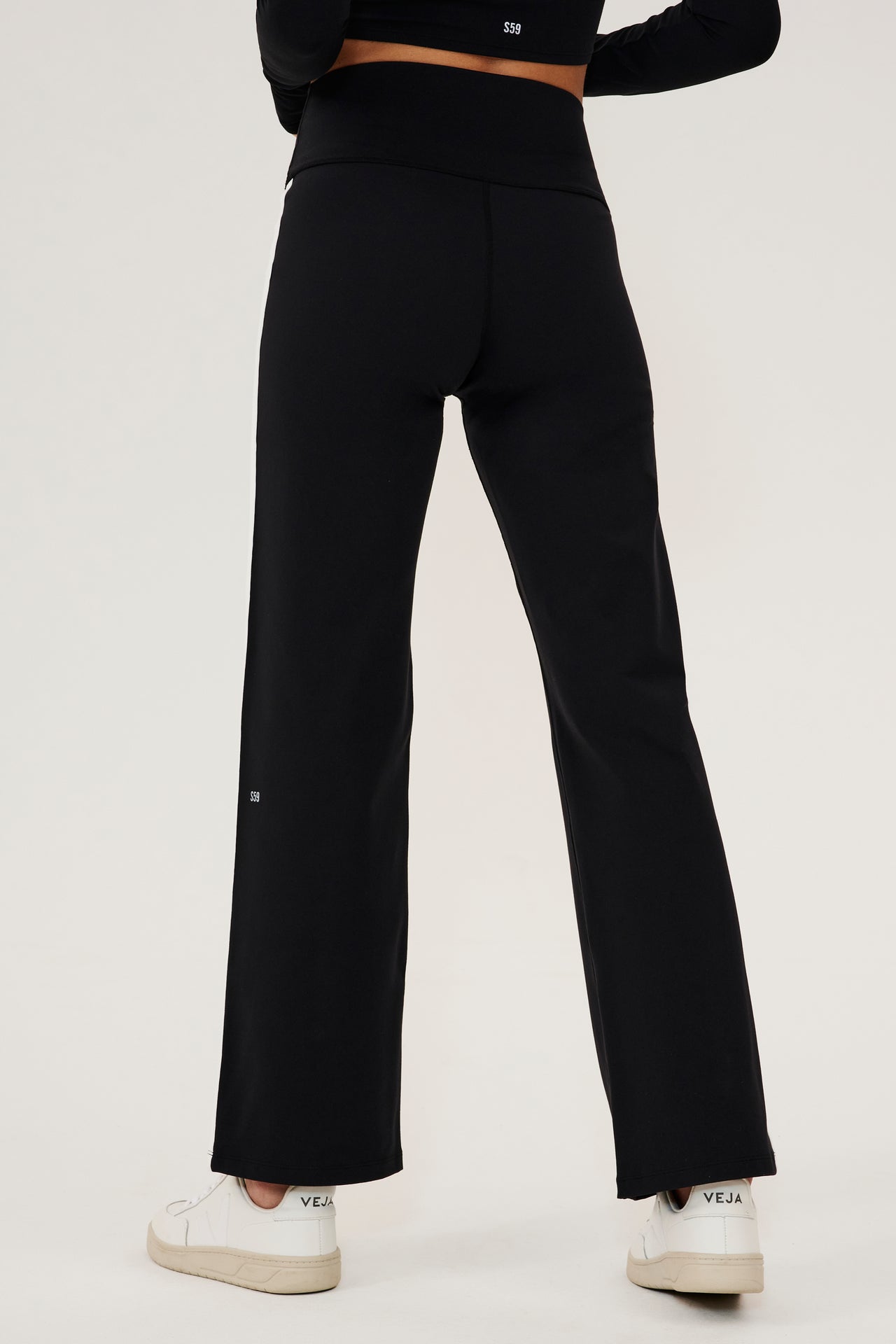 The back view of a woman wearing SPLITS59 Harper Supplex Pant - Black/White with a side stripe.