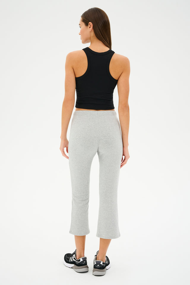 A person wearing the SPLITS59 Brooks Fleece Cropped Flare in Heather Grey, a black sleeveless top, and black sneakers is standing against a plain white background.