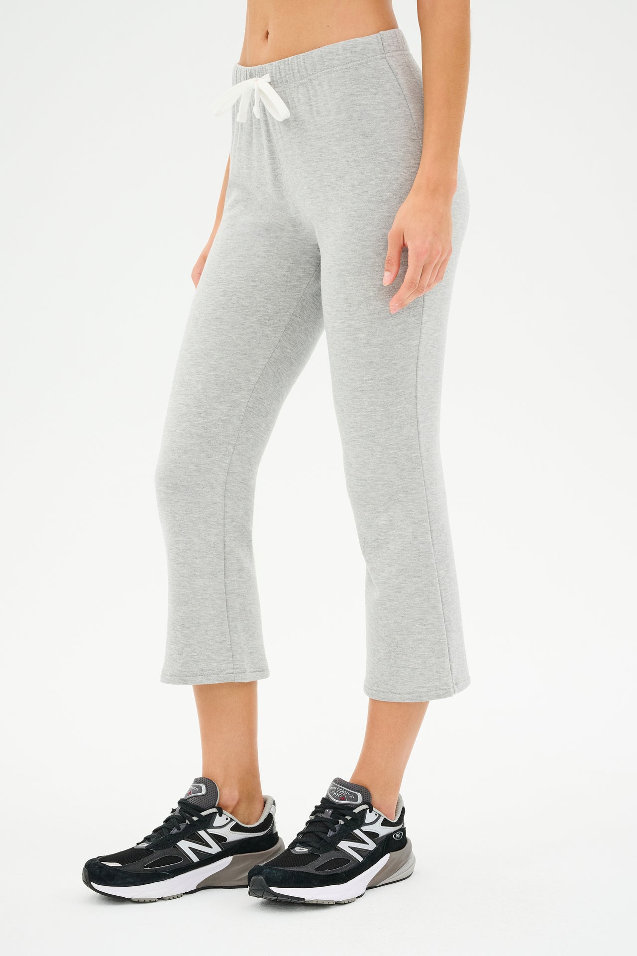 A person wears the SPLITS59 Brooks Fleece Cropped Flare in heather grey with a white drawstring and black running shoes, standing against a plain background, exuding a comfy casual chic vibe.