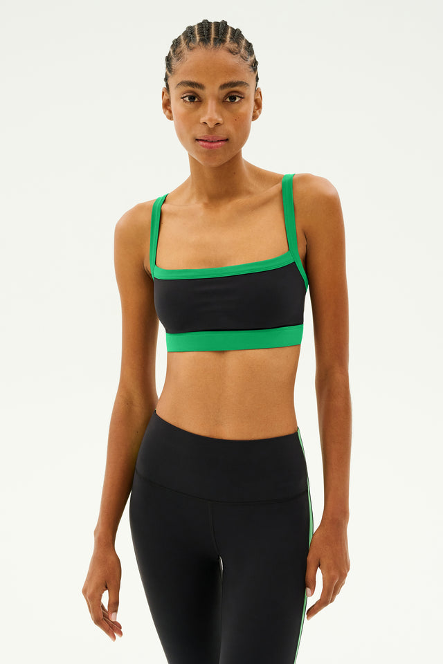 A person wearing the Monah Rigor Bra in black and grass from SPLITS59 sports a sleek spandex ensemble against a plain background.