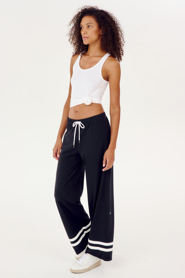 A woman wearing a white tank top and black SPLITS59 Quinn Airweight Wide Leg Pant for comfort.