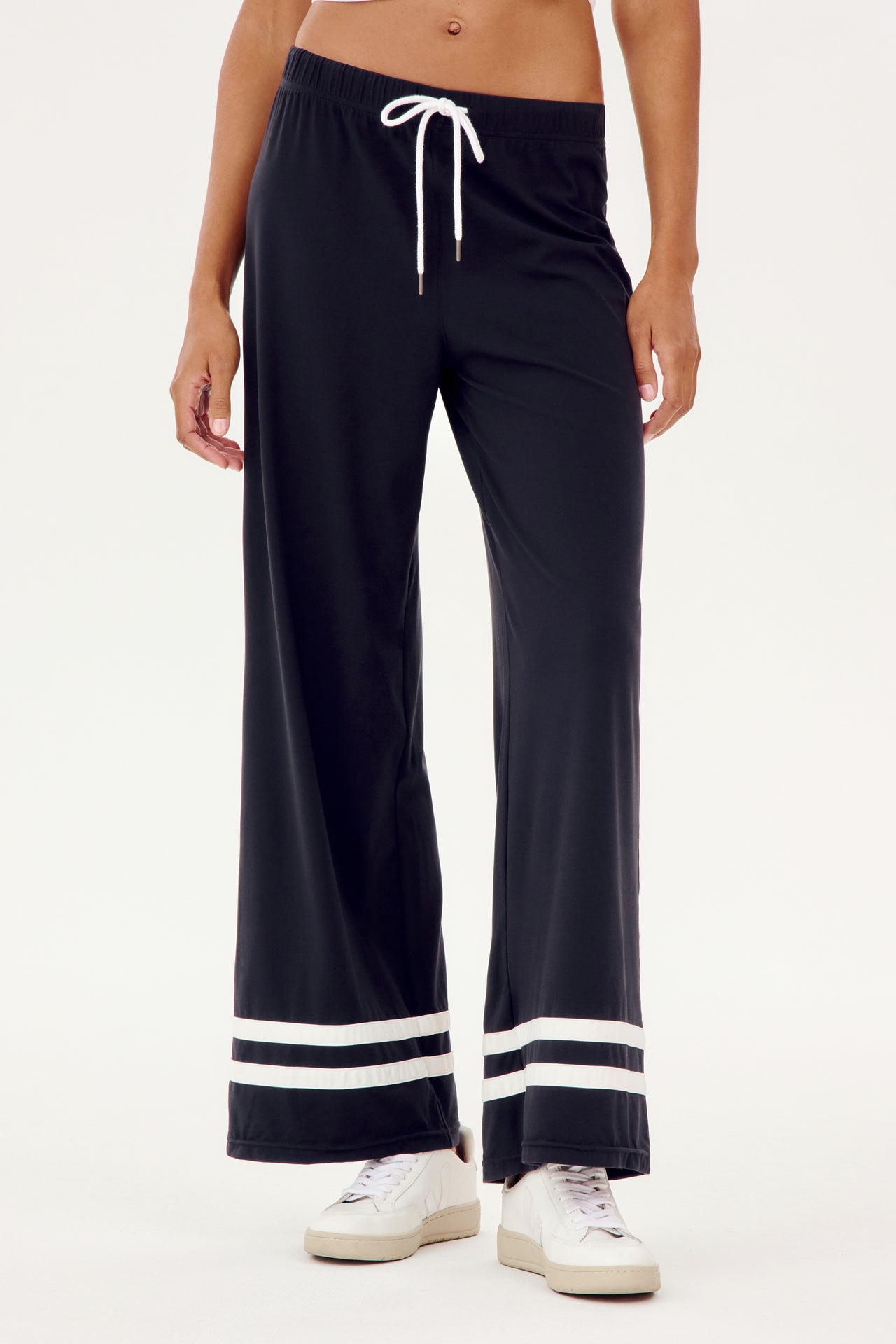 A woman wearing a comfortable black SPLITS59 Quinn Airweight Wide Leg Pant with white stripes designed for workouts.
