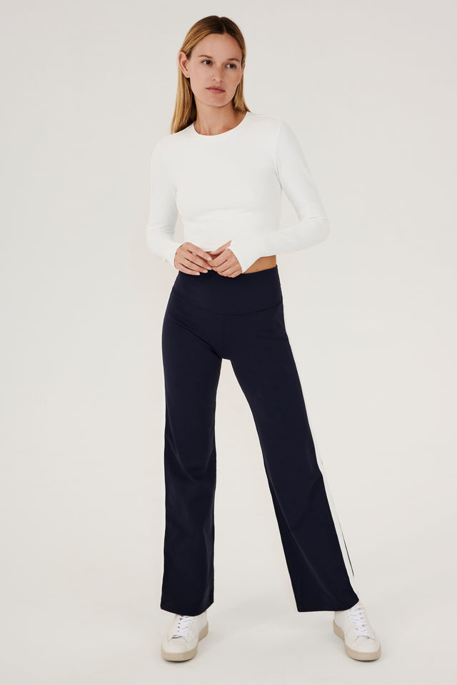 The model is wearing a white top and navy Harper Supplex Pant by SPLITS59.