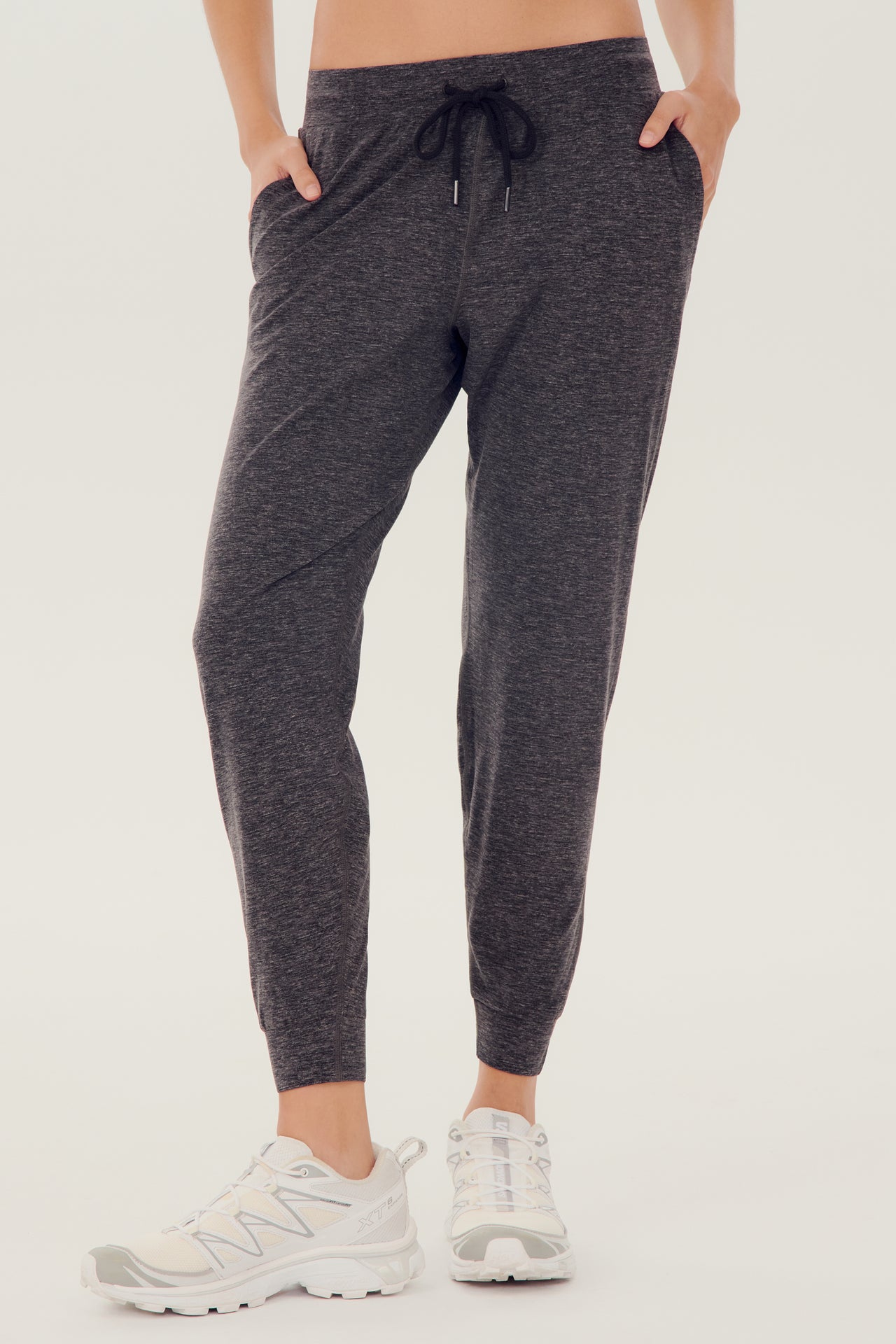 Front view of girl wearing dark grey sweatpants with black tie around waistband with white shoes 
