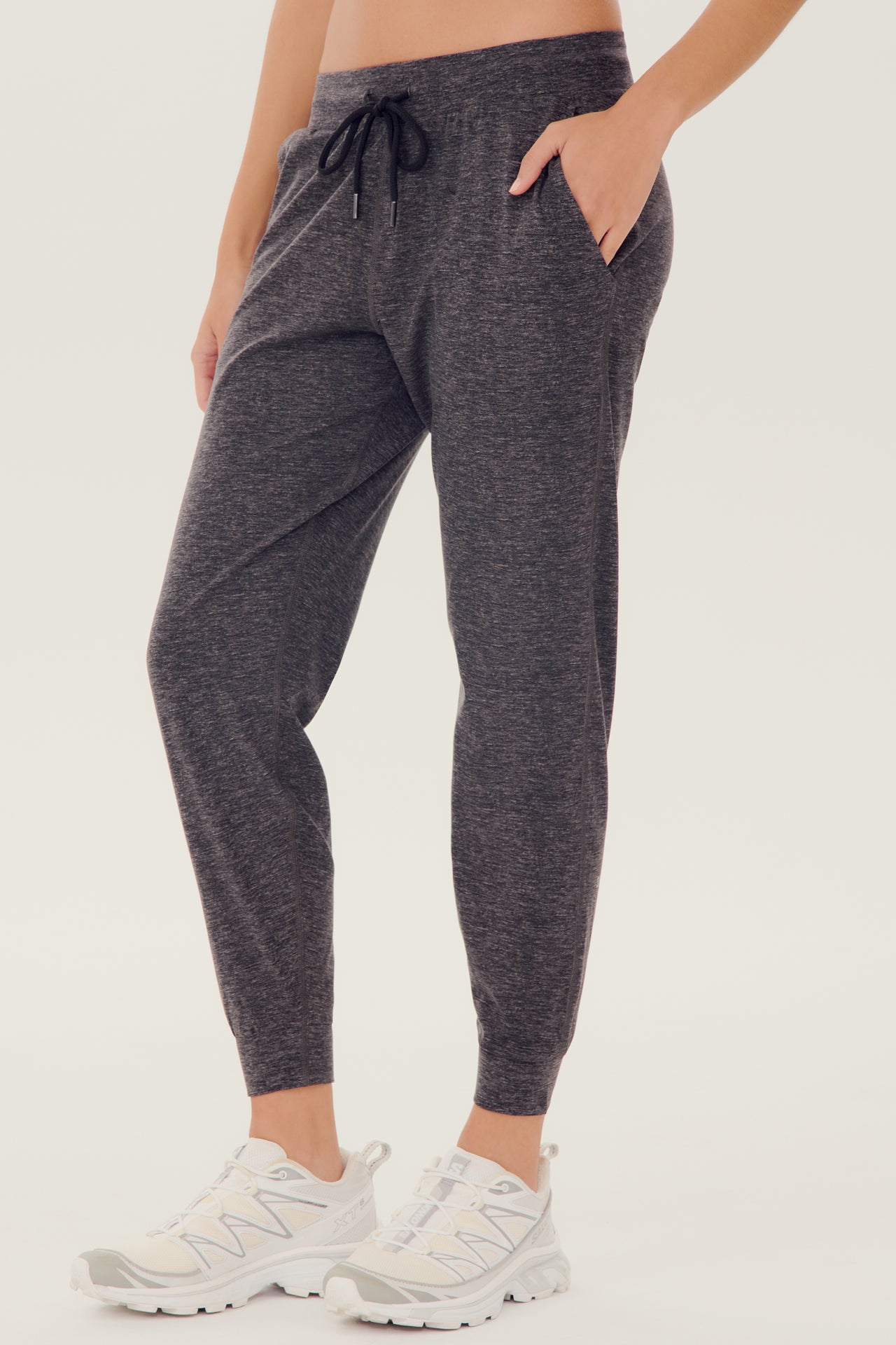 Side view of girl wearing dark grey sweatpants with black tie around waistband with white shoes