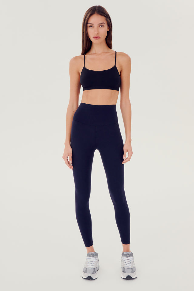 Full front view of girl wearing dark blue leggings right above the ankle with dark blue sports bra grey shoes