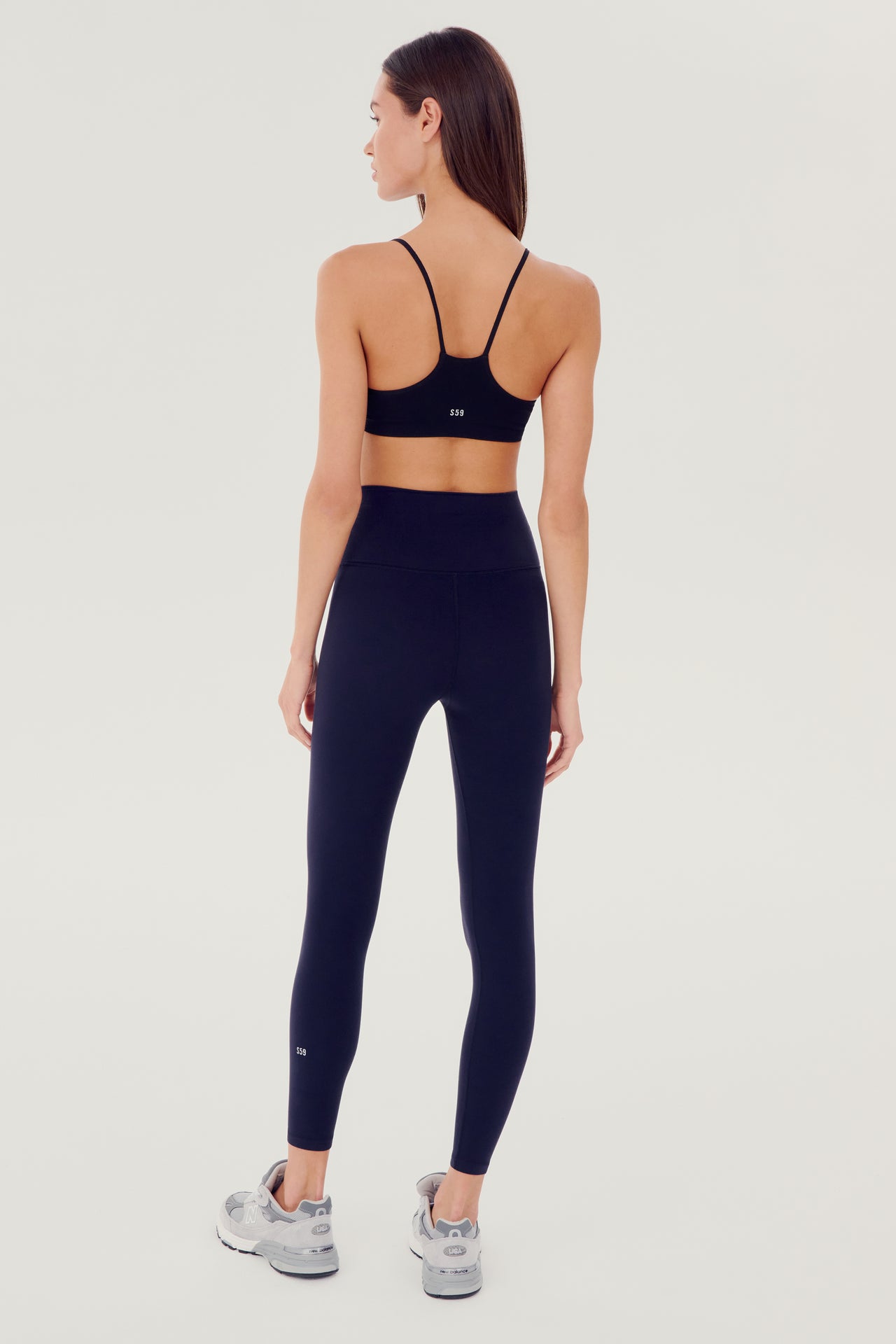 Full back view of girl wearing dark blue leggings right above the ankle with dark blue sports bra grey shoes