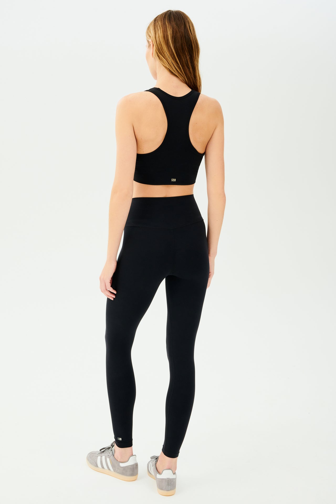 Full back view of girl wearing black sports bra with scrunch and black leggings with grey shoes with 3 stripes