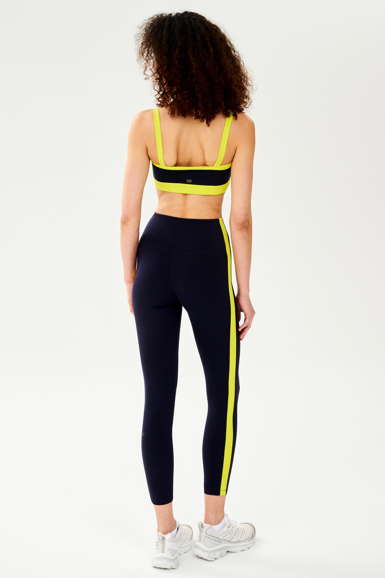 The back view of a woman in comfortable SPLITS59 black and yellow leggings designed for workout support.