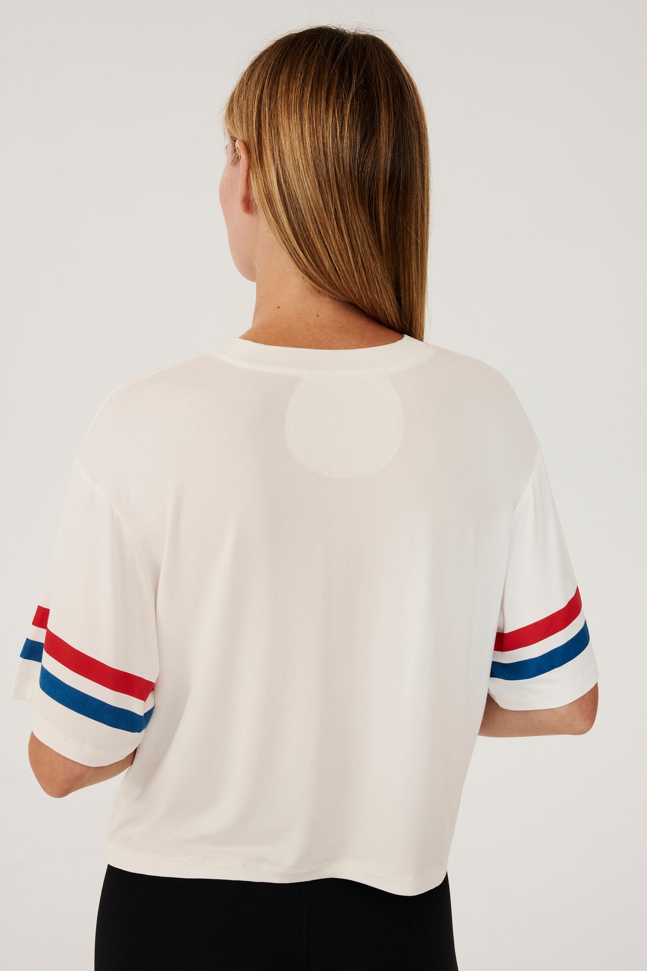 Back view of girl wearing a cropped white shirt with red and blue stripes on the arm and a black leggings 