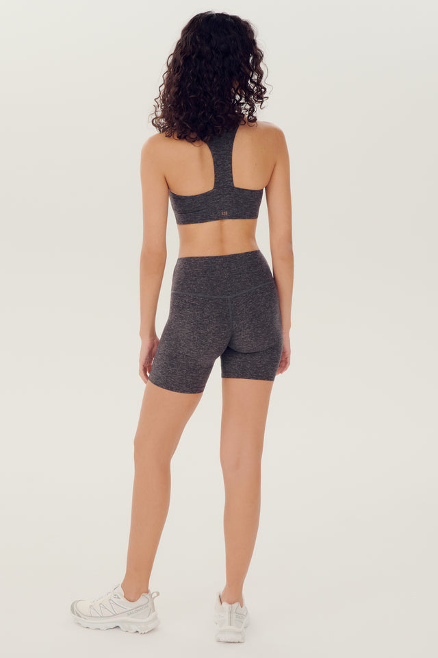 Full back view of girl wearing highwaisted mid thigh grey bike shorts with grey sports bra and white shoes