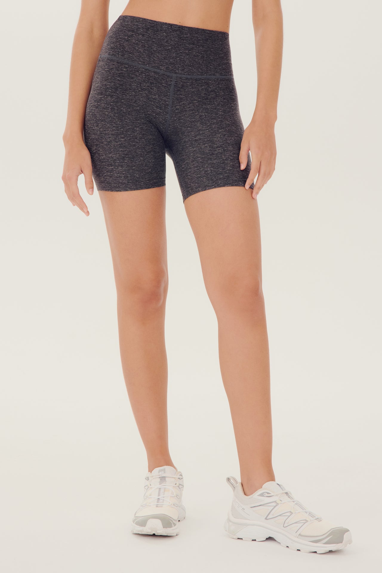 Front view of girl wearing highwaisted mid thigh grey bike shorts withwhite shoes