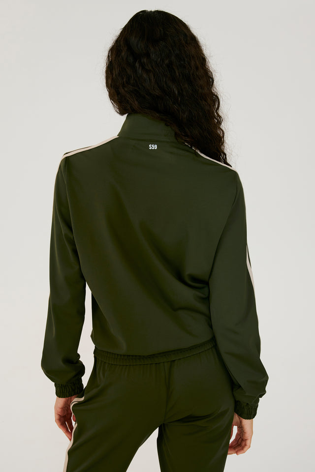 Back view of girl wearing dark green zip jacket that stops under chin with two white stripes down the side and a dark green sweatpants 