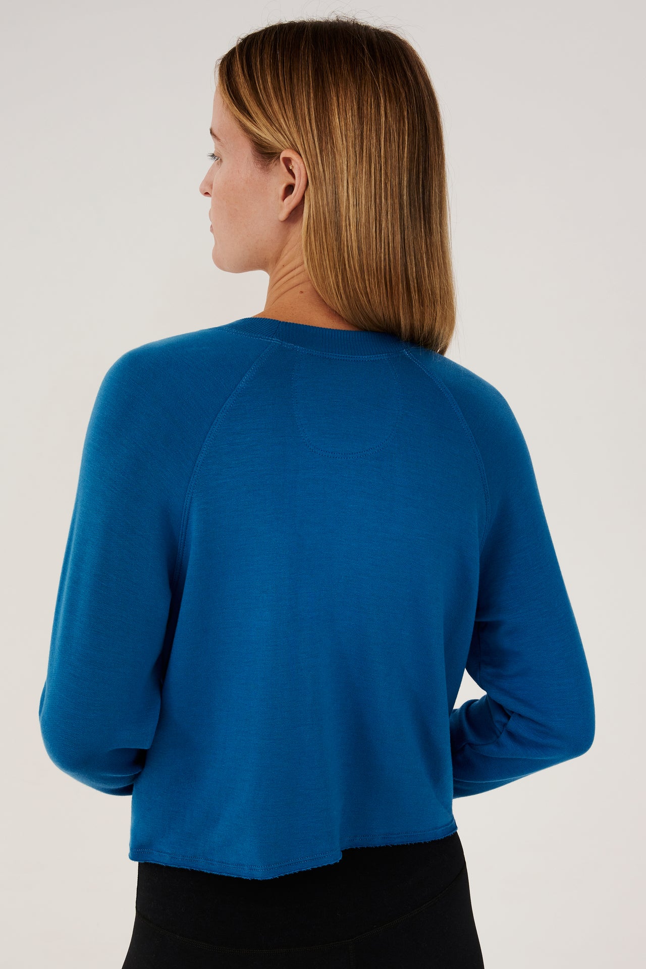 Back view of woman with dark blonde hair, wearing cropped  bright blue sweatshirt with black leggings