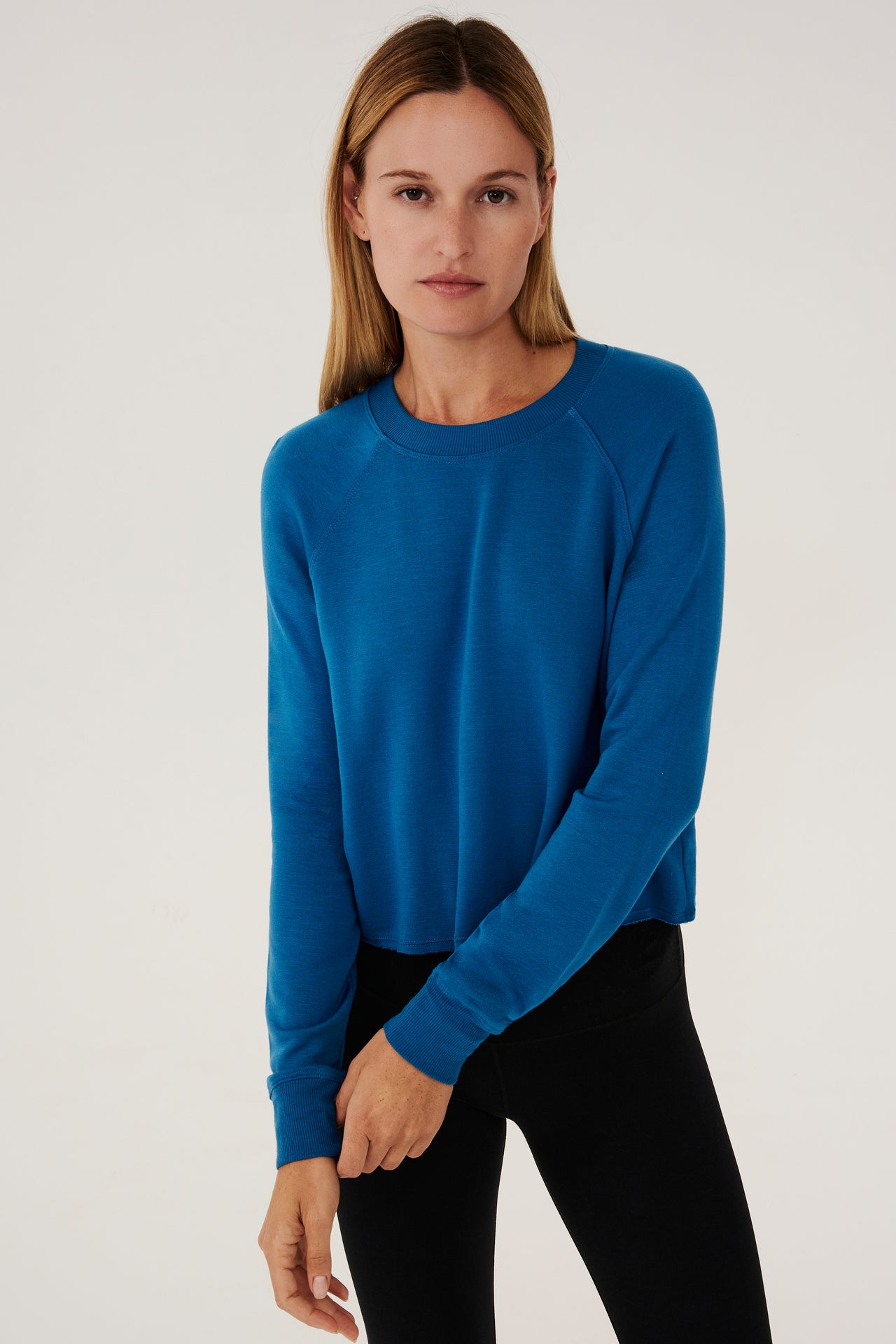 Front view of woman with dark blonde hair, wearing  bright  cropped blue sweatshirt with black leggings