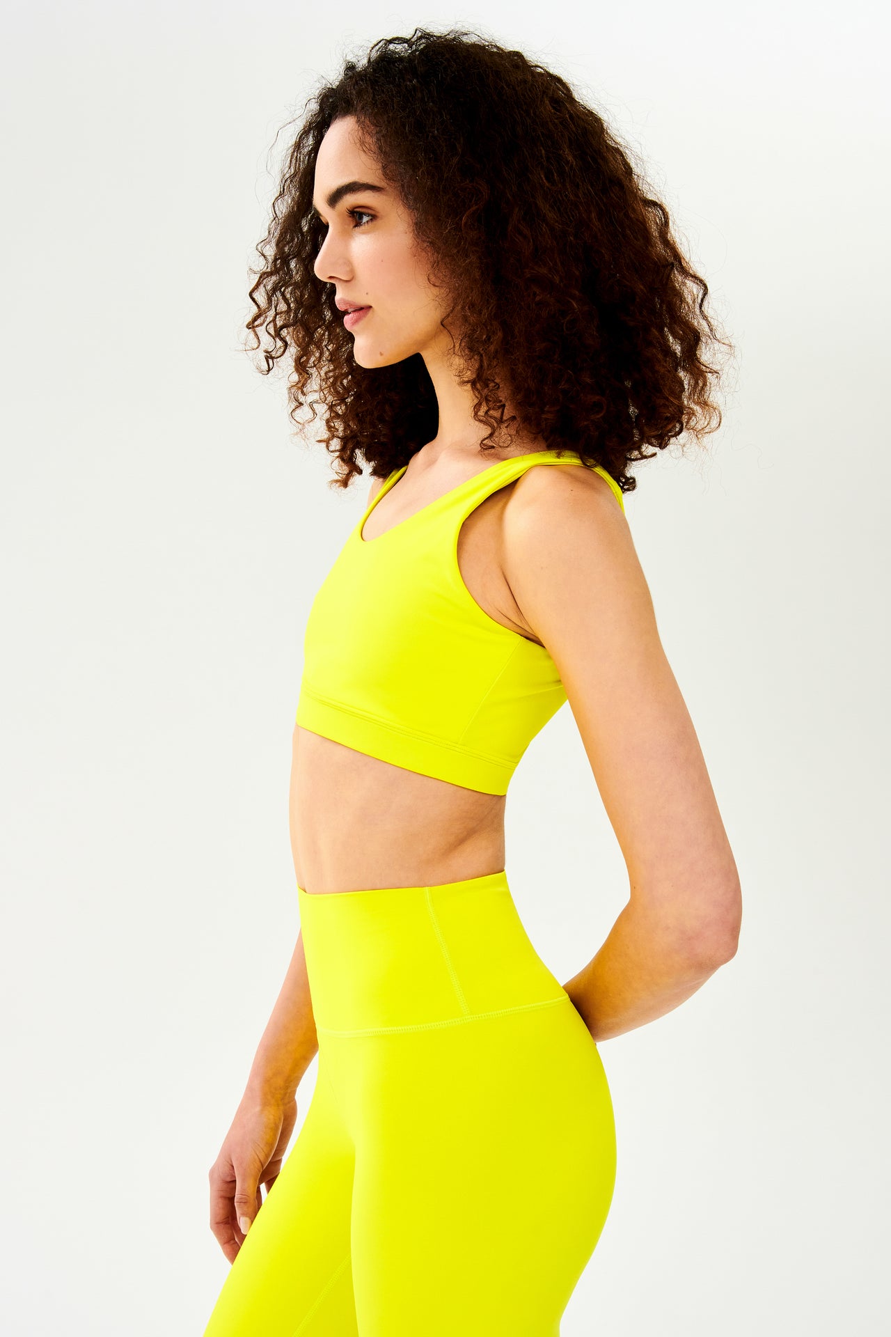 Front side view of woman with curly dark wearing bright yellow bra with bright yellow leggings
